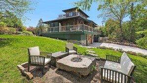 A large house with a deck, outdoor seating, and a fire pit. - Designer Home with Wraparound Porches & Fire Pit (Bourne)