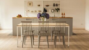 Un coin repas avec une table, des chaises, un vase de fleurs et, au fond, une cuisine.