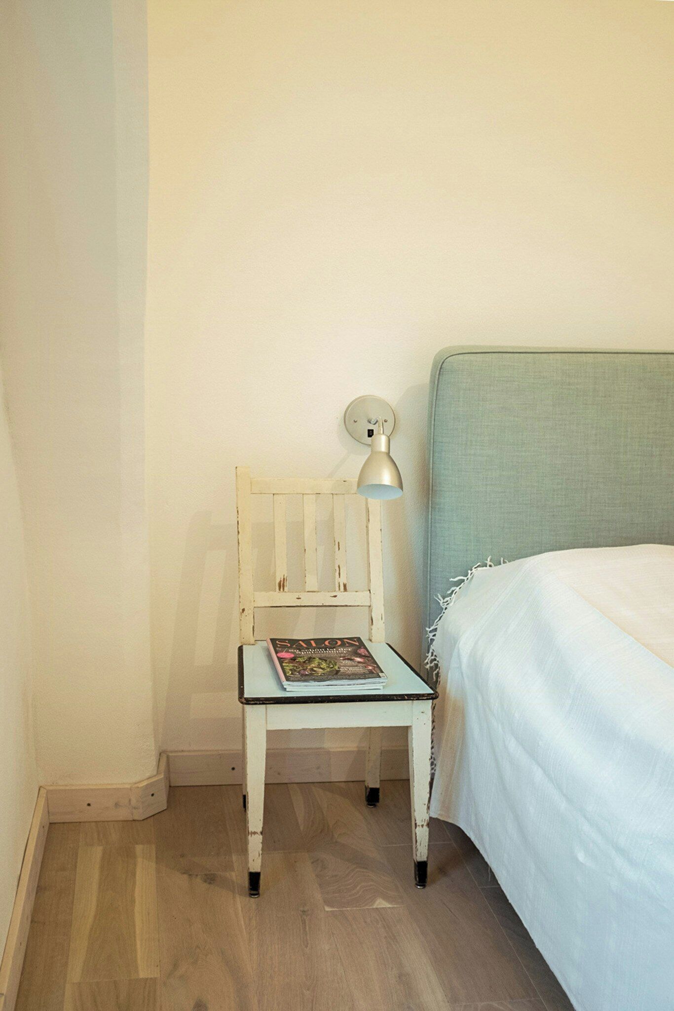 Una habitación pequeña con una cama, una silla y una mesa con lámpara.