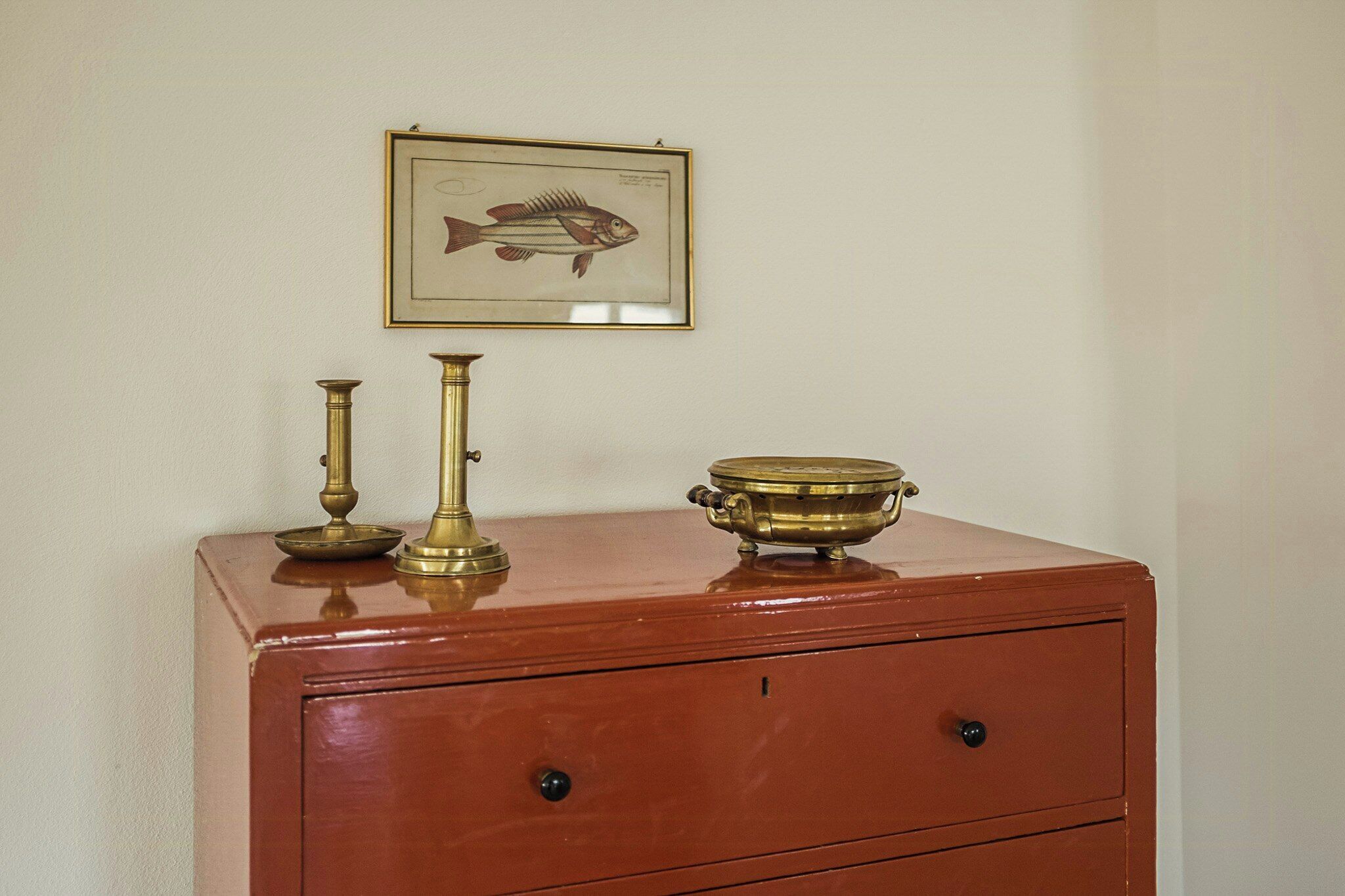 A wooden cabinet with brass objects and a framed fish illustration.