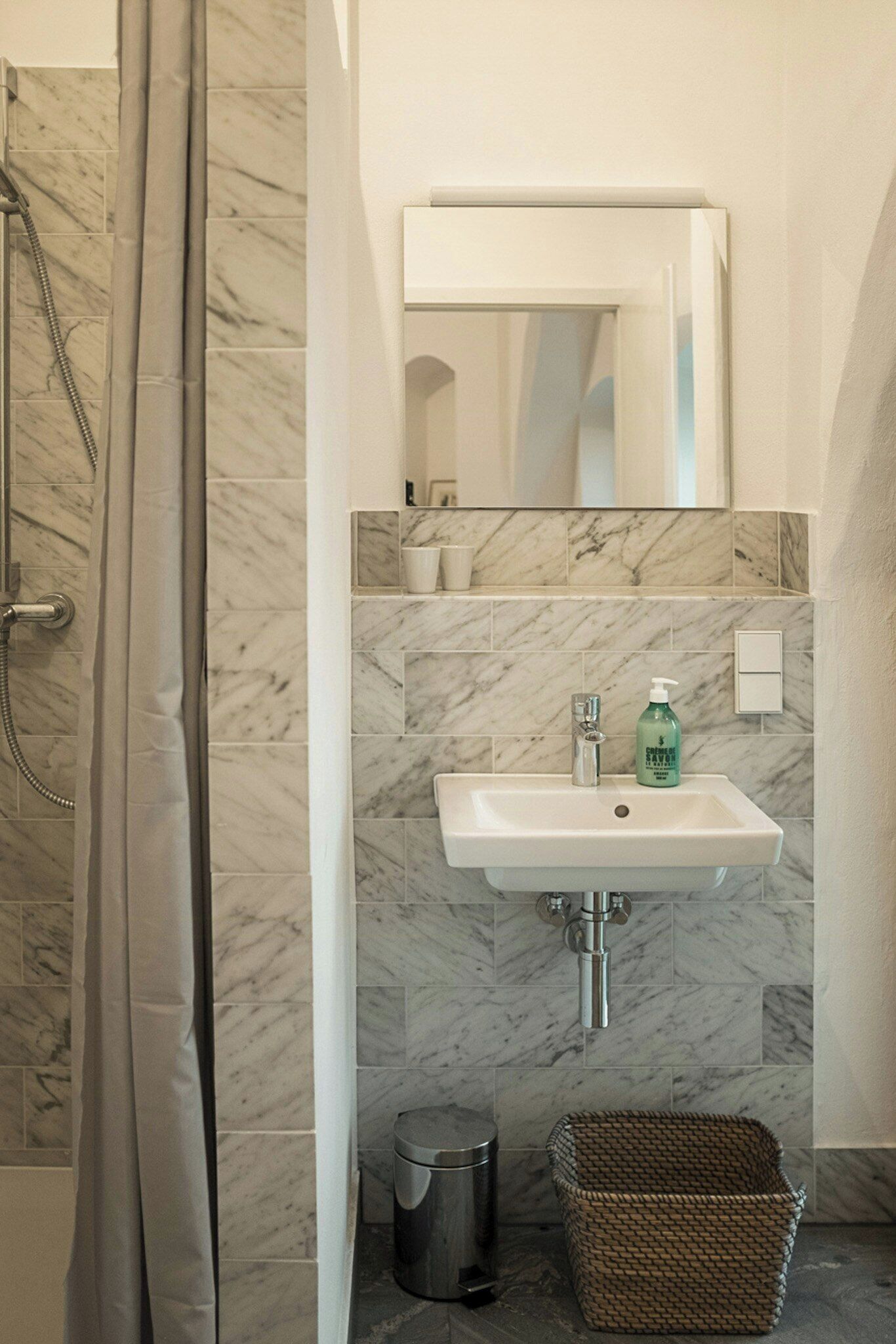 Een badkamer met een douche, een wastafel, een spiegel en een prullenbak.
