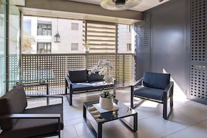 Ein moderner Balkon mit einer Couch, Stühlen und einem Couchtisch, mit Blick auf Gebäude und einem dekorativen Zaun.