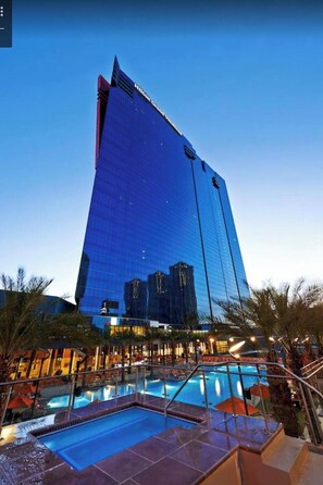 Un hotel moderno con un amplio frente de vidrio, una zona de piscina y palmeras.