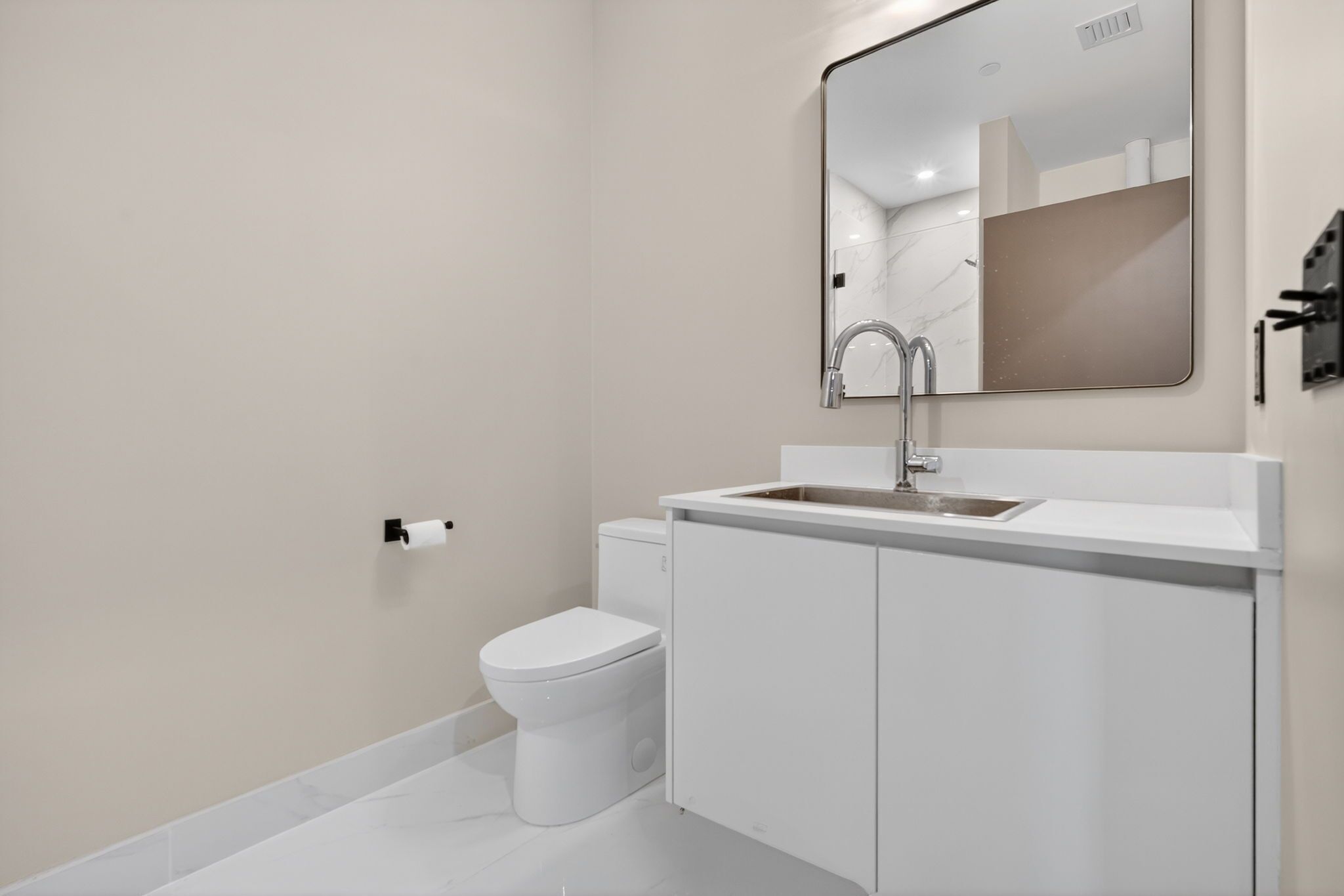 Een moderne badkamer met een wit toilet, een wastafel met een spiegel erboven en een toiletrolhouder aan de muur.