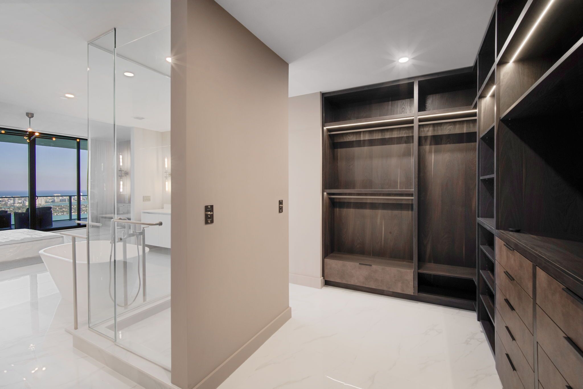 Un baño moderno con cabina de ducha de vidrio, una bañera grande y un vestidor con estanterías de madera.