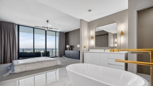 Een moderne hotelkamer met een groot bad, een groot bed, een kaptafel met spiegel en uitzicht op de stad.