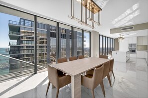 A modern dining area with a large table and chairs, large windows, and a view of the city. - Waterfront Opulent Sky Penthouse - Aria Reserve (Miami)