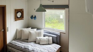 Een slaapkamer met een bed, een raam, een wandplank met spullen en een deur.