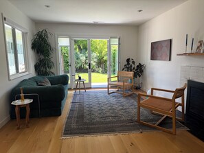 A living room with a green sofa, a wooden chair, a small table, and a fireplace. - Sunny Garden Oasis in perfect Mill Valley (Mill Valley)