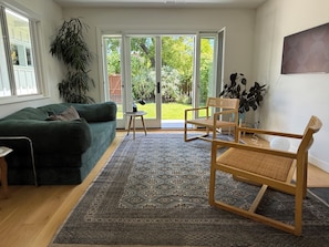 A living room with a green sofa, a wooden chair, a patterned rug, and a view through glass doors to a garden. - Sunny Garden Oasis in perfect Mill Valley (Mill Valley)