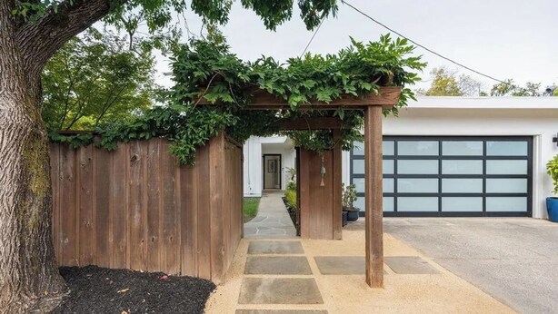 Eine Holz-Pergola mit Kletterpflanzen, ein Steinweg und eine Garagentür.