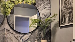 A bathroom with a marble backsplash, a round mirror, a sink, a toilet, and a potted plant. - City Centre Sanctuary, with free parking. (Worcester)