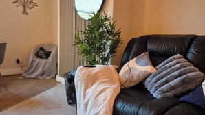 A living room with a black leather sofa, a mirror, a potted plant, and a wall with vertical lines. - City Centre Sanctuary, with free parking. (Worcester)