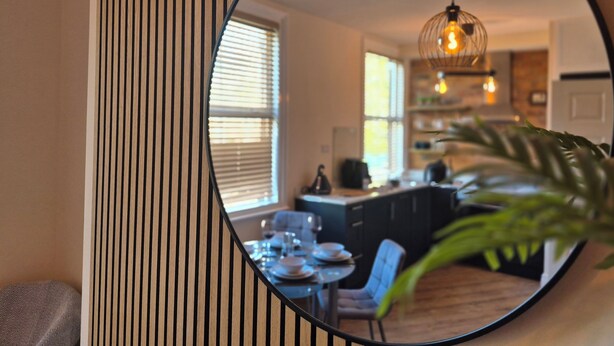 A round mirror reflecting a dining area with a table, chairs, and a hanging light fixture. - City Centre Sanctuary, with free parking. (Worcester)