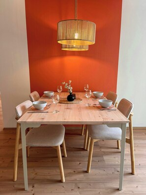 Uma mesa de jantar com seis cadeiras, um vaso com flores e um lustre.