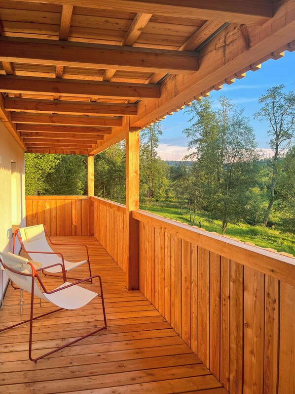 A wooden deck with two lounge chairs, a wooden railing, and a view of a forested landscape. - Hideaway by the stream with countryside views (Jandelsbrunn)
