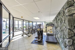 Un gimnasio con equipo de ejercicio, ventanas amplias y una pared de piedra.