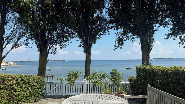 A wooden bench and table in a shaded outdoor area with a view of the sea and boats. - Town house with sea view in historic Ærøskøbing (Ærøskøbing)