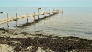 En träbrygga som sträcker sig ut i stilla vatten, med en sandstrand i förgrunden.