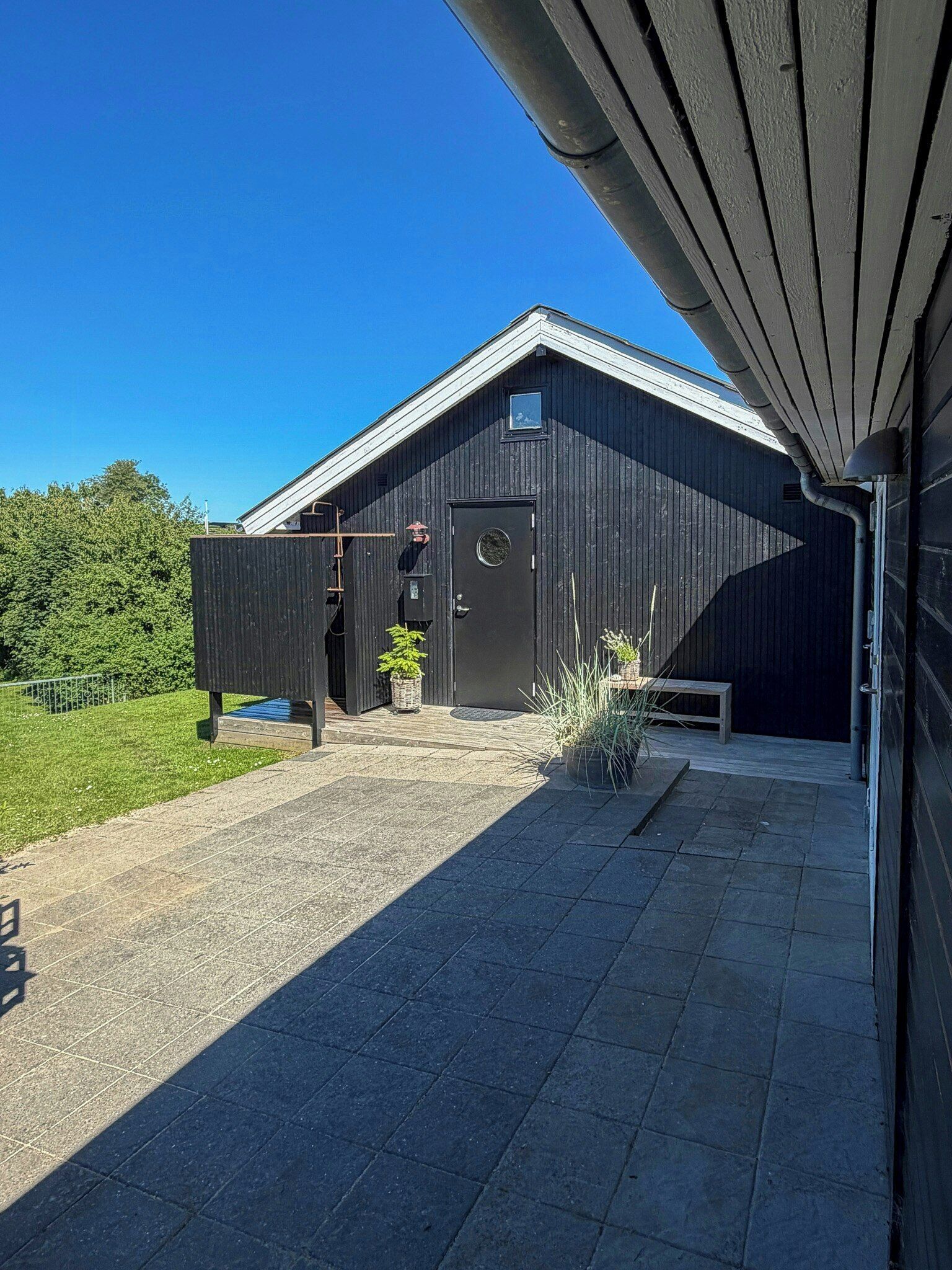 A modern building with a sloped roof, a small entrance, and a paved area with potted plants.