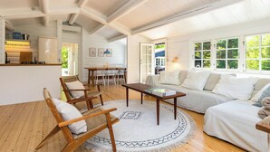 A room with a wooden floor, a round rug, a sofa, a coffee table, and a dining area with chairs and a table. - Log cabin with pool near Tisvilde (Vejby)