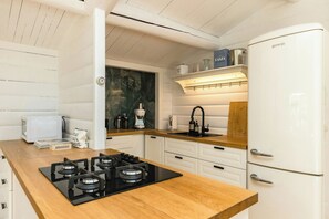 A kitchen with a gas stove, white cabinets, a refrigerator, and a wooden countertop. - Log cabin with pool near Tisvilde (Vejby)