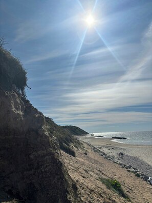 Ein Strand mit einer felsigen Klippe, blauem Himmel und Sonnenschein.
