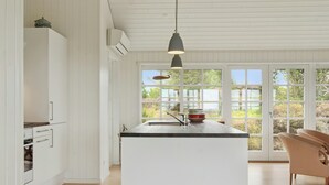 Una cocina moderna con una isla central, armarios blancos y un ventanal con vistas a zonas verdes.