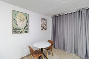 A room with a round table, two chairs, a grey curtain, and two floral paintings on the wall. - Boutique Hotel-Style Room In Ferndale-H8 (Randburg)