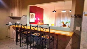 A modern kitchen with a bar area, including a dining table with chairs, a large mirror, pendant lights, and a vase with flowers. - The Cozy Three Bedroom Home With Back up Water (Johannesburg)