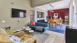 A living room with a TV, sofa, coffee table, and dining area with chairs and a table. - The Cozy Three Bedroom Home With Back up Water (Johannesburg)
