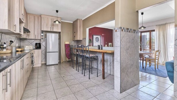 A modern kitchen with a refrigerator, wooden cabinets, and a dining area with chairs and a table. - The Cozy Three Bedroom Home With Back up Water (Johannesburg)