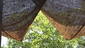 A covered outdoor seating area with a table and chairs, a view of a tree, and a building in the background. - The Grange in Cantal (Parlan)