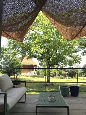 A covered outdoor seating area with a table and chairs, a view of a tree, and a building in the background. - The Grange in Cantal (Parlan)