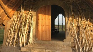 An arched wooden door leading to a room with a stone wall and a view of trees. - The Grange in Cantal (Parlan)