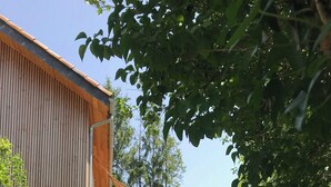 A building with a wooden exterior, a balcony with outdoor seating, and a gravel path leading to the entrance. - The Grange in Cantal (Parlan)