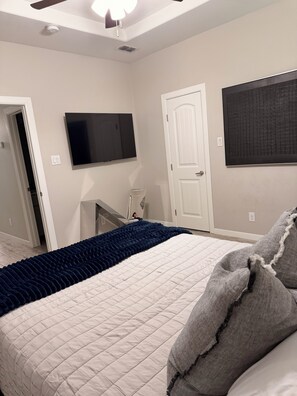Un dormitorio con una cama, televisión en la pared, una puerta y una ventana.