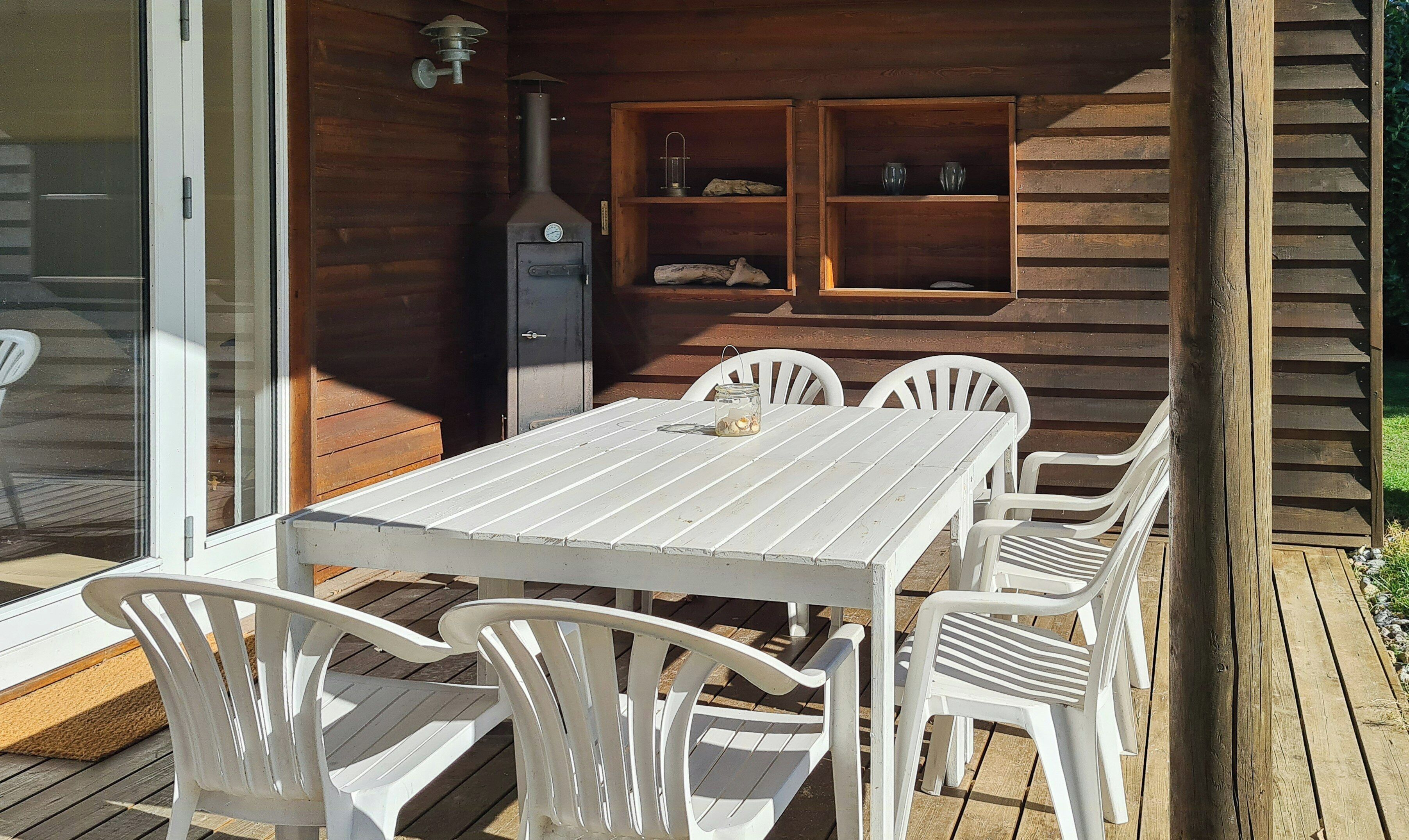 A wooden deck with a white table and chairs, a barbecue grill, and shelves with items.