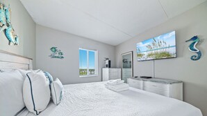 Ein Schlafzimmer mit einem großen Bett, einem Schminktisch, einem Fernseher und dekorativen Wandbildern.