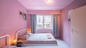 Un dormitorio con dos camas, una ventana con cortinas, una planta en la pared y una puerta.