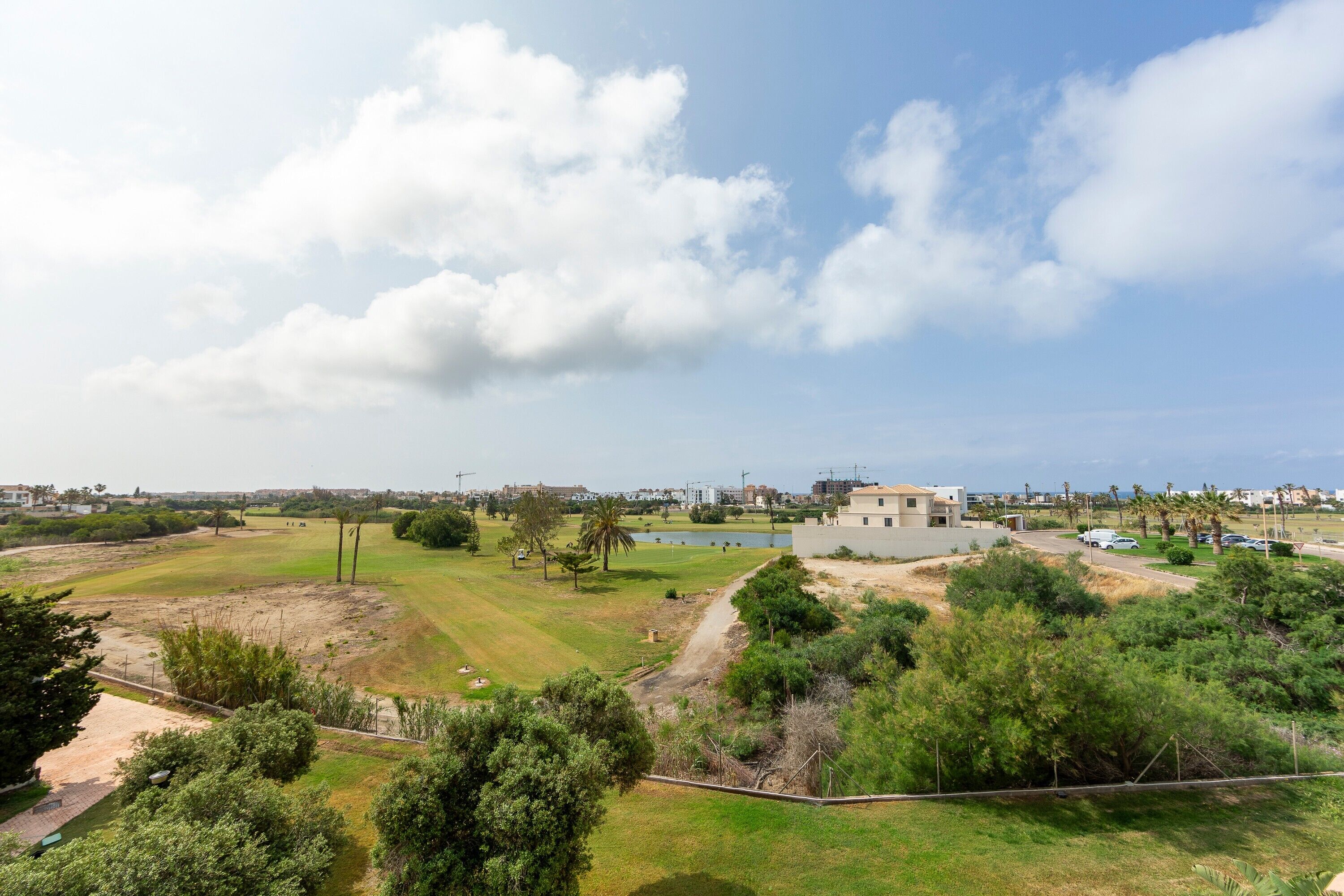 Un campo de golf con un edificio, árboles y cielo despejado.