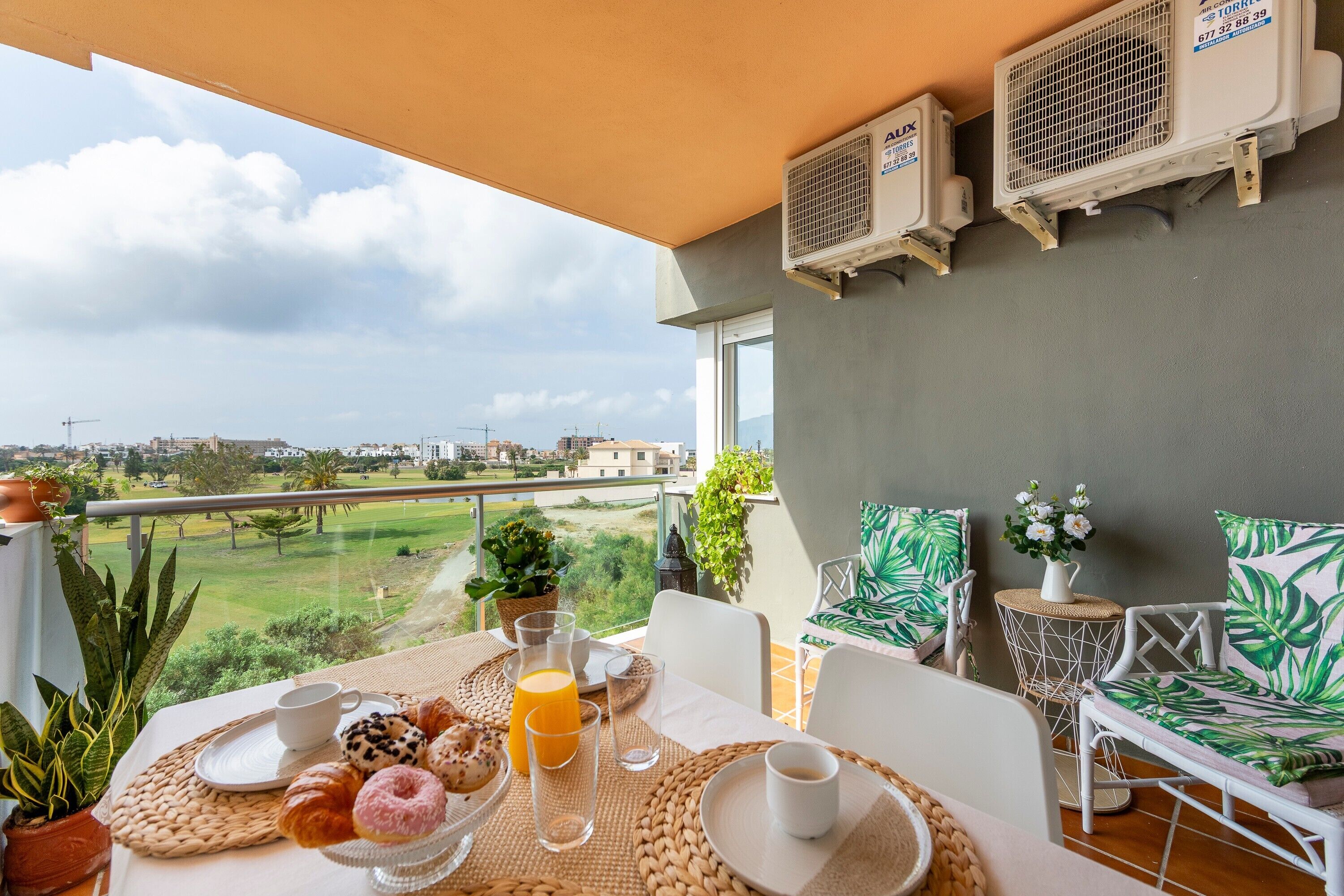 A balcony with a table set for breakfast, air conditioning units, and a view of a golf course.