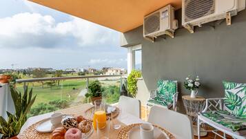 A balcony with a table set for breakfast, air conditioning units, and a view of a golf course.