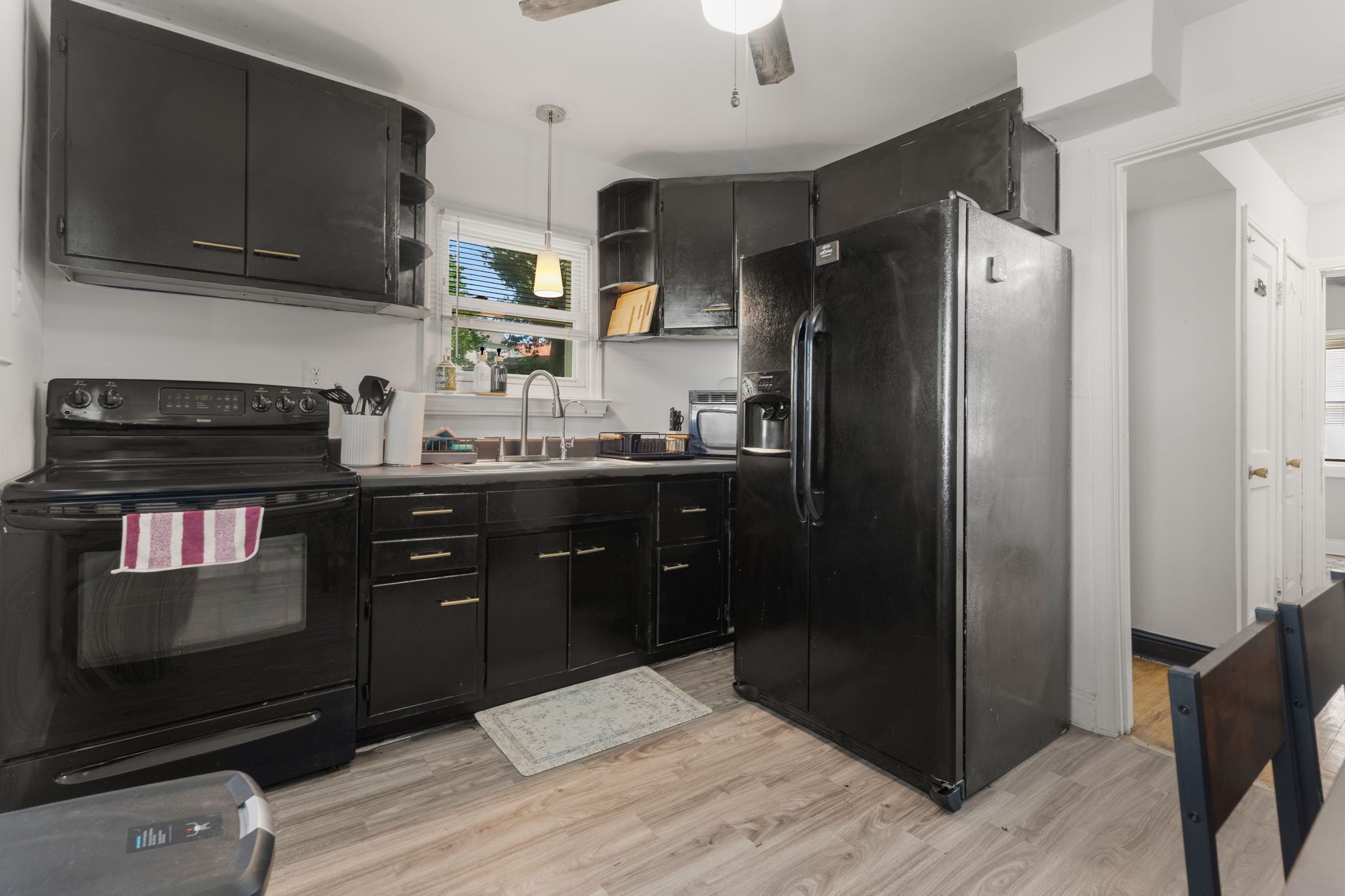 Una cocina con gabinetes negros, un refrigerador de acero inoxidable, una estufa y una ventana con persianas.