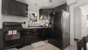 Una cocina con gabinetes negros, un refrigerador de acero inoxidable, una estufa y una ventana con persianas.