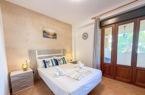 Ein Hotelzimmer mit Bett, Nachttischen, Wanduhr und Blick durch eine Glastür.