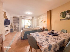Ein Zimmer mit einem Bett, einem Esstisch mit Stühlen, einem Fernseher, einem Bücherregal und einem Gemälde an der Wand.