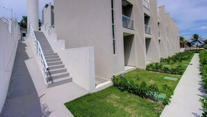 A modern building with a staircase leading to a flat-roofed structure, surrounded by a well-maintained lawn and a row of palm trees. - Beach Townhouses I - Triplex by Carpediem (Aquiraz)