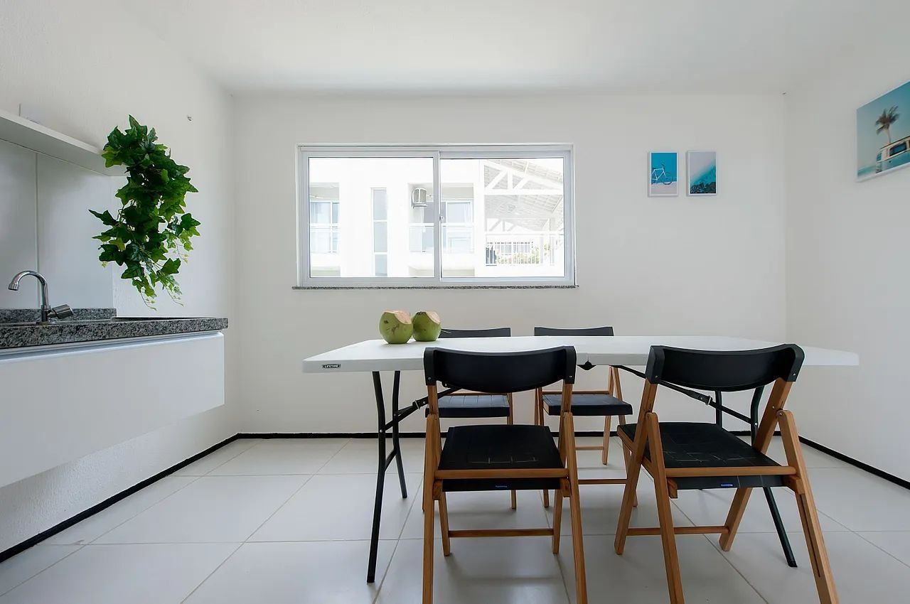 A modern kitchen with a white countertop, two black chairs, a white table, and a window with a view of a building.
