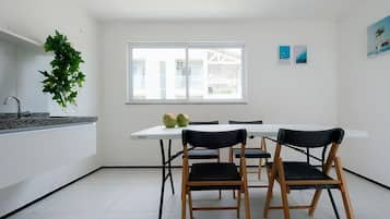 Una cocina moderna con una encimera blanca, dos sillas negras, una mesa blanca y un ventanal con vistas a un edificio.